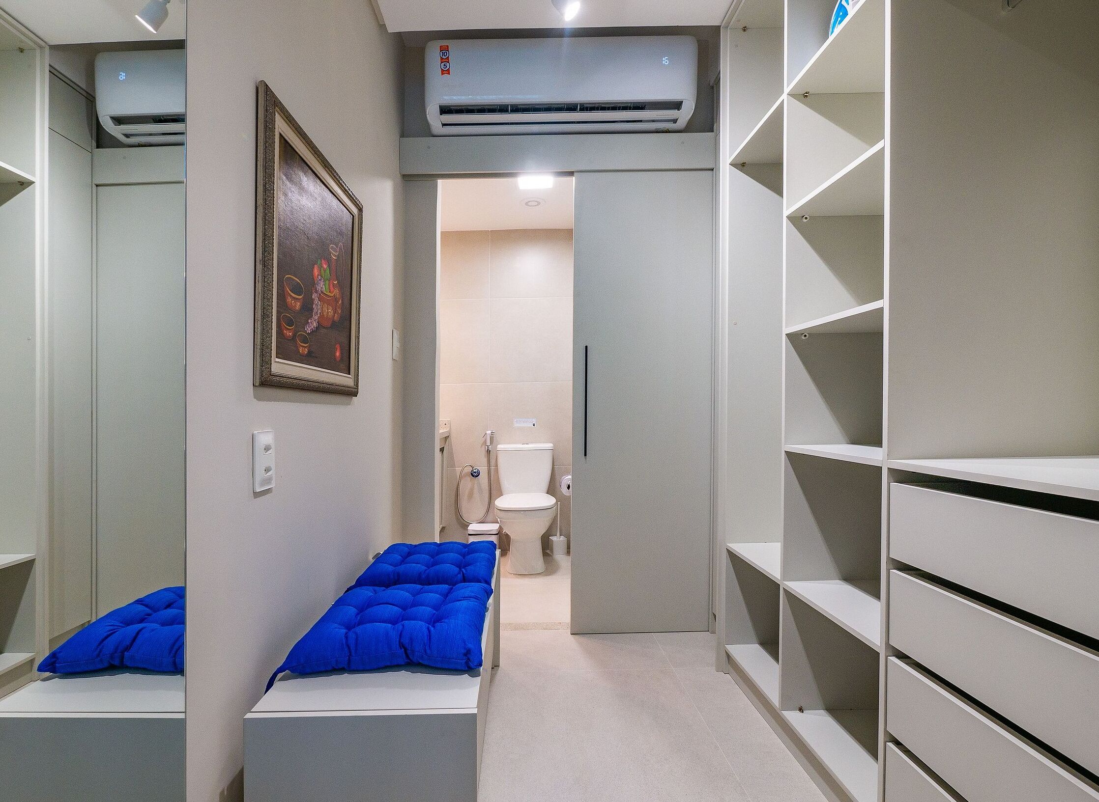 Een smalle gang met een bed, een toilet en een grote airconditioning unit erboven.