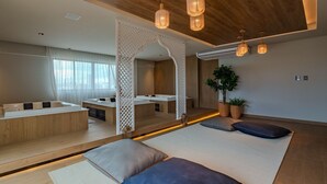 A modern spa room with wooden flooring, a large mirror, and a seating area with cushions.