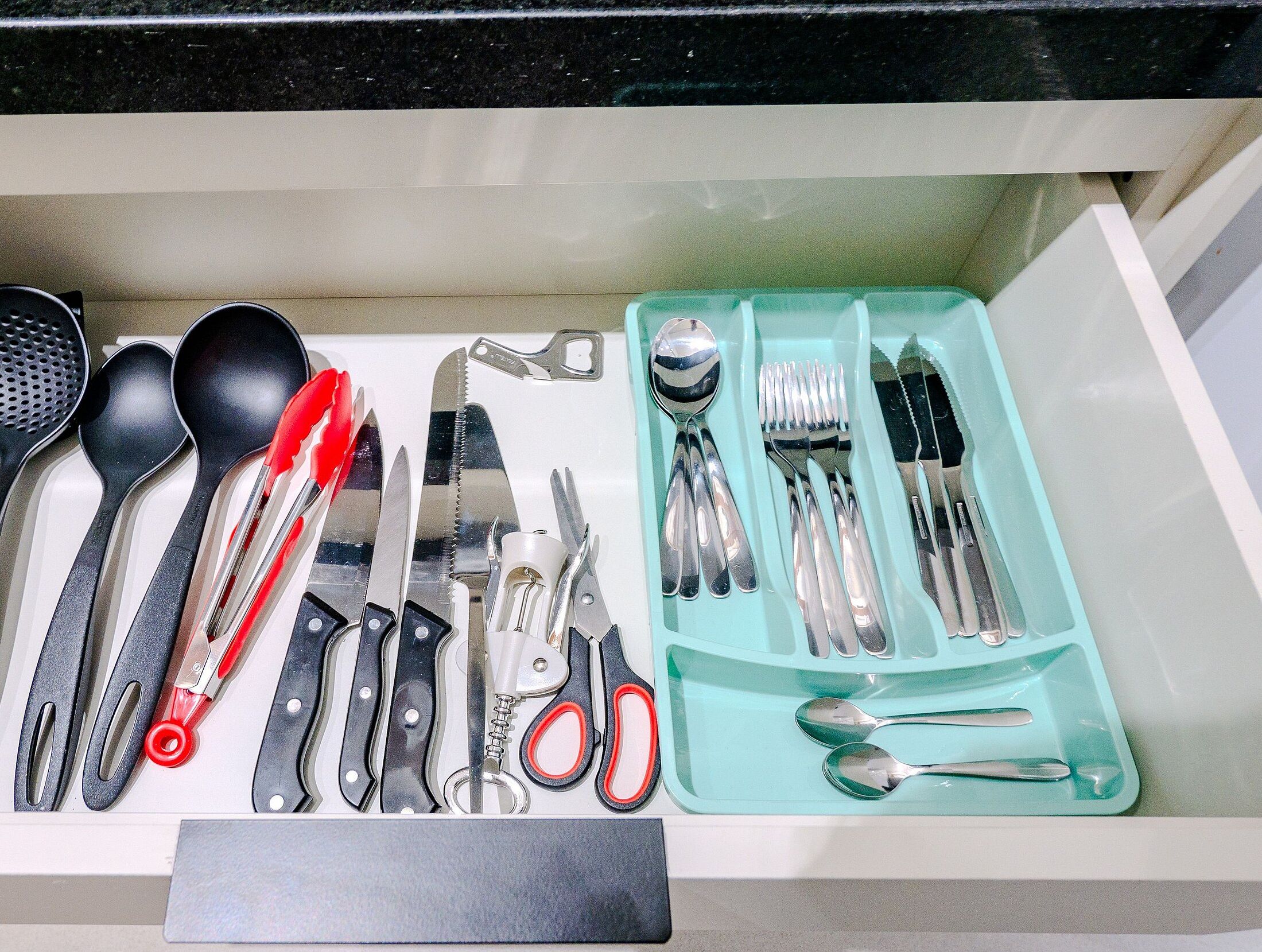 Un cajón con diversos utensilios y herramientas de cocina, como cucharas, cuchillos y tijeras.