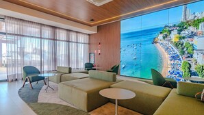 A modern hotel lobby with green sofas, a small round table, and a large window overlooking a beach.