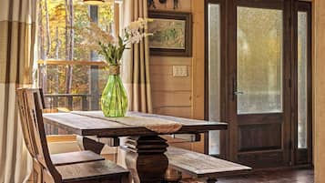 Une table de salle à manger en bois, des chaises, un vase avec des fleurs, une carte encadrée et une porte en bois avec un panneau en verre.