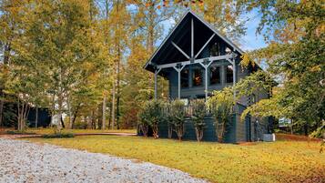 A cabin with a triangular roof, surrounded by trees and a gravel path.
