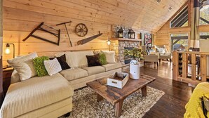 A cozy cabin interior with a wooden ceiling, a sofa, a coffee table, and a stone fireplace. - Charming Cabin Retreat • Pet-Friendly & Trails (Sevierville)
