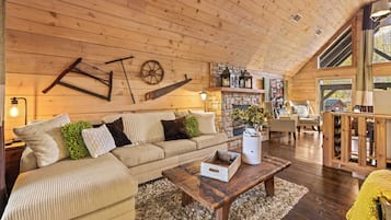 L’intérieur chaleureux d’un chalet avec un plafond en bois, un canapé, une table basse et une cheminée en pierre.