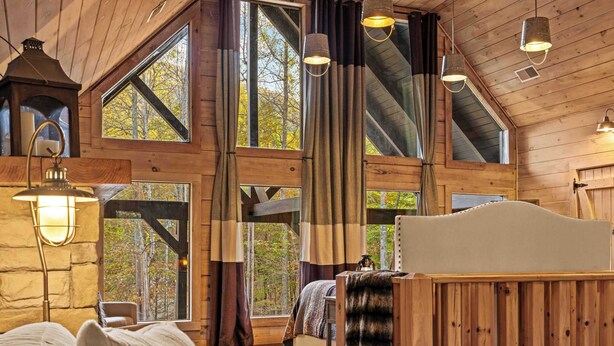 A cabin interior with a loft bed, large windows, wooden beams, and hanging light fixtures. - Charming Cabin Retreat • Pet-Friendly & Trails (Sevierville)