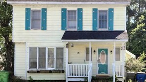 A two-story house with a porch, a front door with a decorative panel, and a small window with shutters.