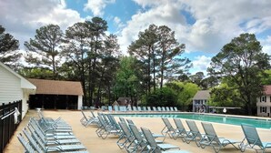 A pool area with lounge chairs and a small table, surrounded by trees and buildings.