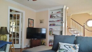 A living room with a sofa, a flat-screen TV, a bookshelf, and a staircase.