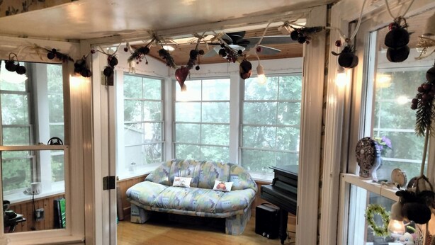 A cozy room with a patterned sofa, a piano, and large windows offering a view of trees.