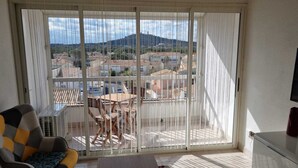 Een balkon met uitzicht op een stad en bergen. Er staat een tafel en stoelen op het balkon.