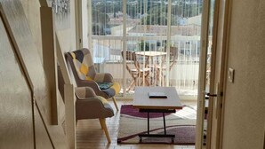 Een gang die uitkomt op een balkon met een tafel en stoelen, een trap en een uitzicht op de stad.