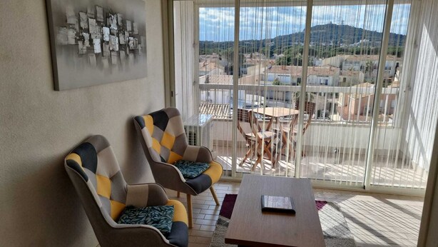 Een balkon met twee fauteuils, een tafeltje en uitzicht op gebouwen en heuvels.
