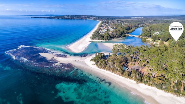 Vista aérea de la bahía Jervis con aguas azul cristalino, una playa arenosa y vegetación exuberante.
