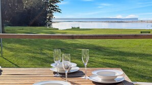 Una mesa servida con copas de vino y platos, con vistas a un área cubierta de césped y una masa de agua.