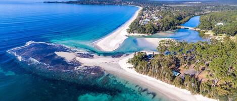 An aerial view of Jervis Bay with clear blue waters, a sandy beach, and lush greenery.