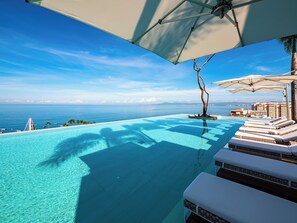 A infinity pool with clear blue water, lounge chairs, and umbrellas. - Pier 57 Luxury | Ocean Views, Infinity Pool & Bar (Puerto Vallarta)
