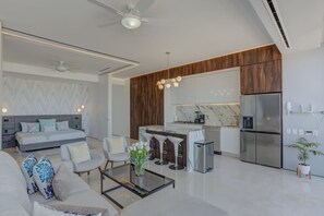 Een moderne woonkamer met een bank, stoelen, een salontafel en een eethoek, met een keuken op de achtergrond.