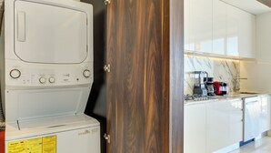 A modern kitchen with white appliances, a wooden door, and a marble backsplash. - Pier 57 Luxury | Ocean Views, Infinity Pool & Bar (Puerto Vallarta)