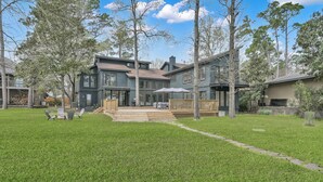 A modern two-story house with a large backyard, a wooden deck, and a covered outdoor seating area.