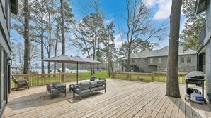 A wooden deck with outdoor furniture, a covered seating area, and a view of a stone building and trees.
