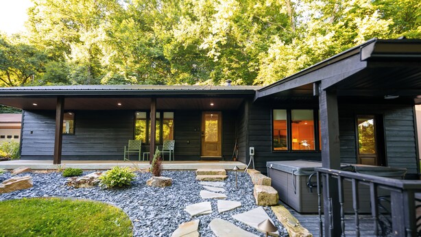 Une maison moderne avec un chemin de pierre menant à une terrasse en bois et à un espace extérieur aménagé et couvert.