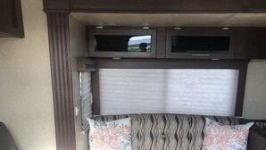 A cozy RV interior with a brown leather sofa, patterned cushions, a small TV, and a window with blinds. - Cozy caravan with WiFi and AC in charming Thermal.Private location (Thermal)