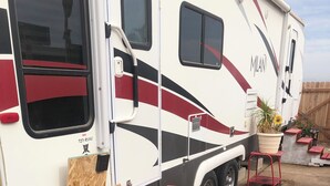 A recreational vehicle with a ramp leading to the entrance, a potted plant, and a small table with a chair. - Cozy caravan with WiFi and AC in charming Thermal.Private location (Thermal)