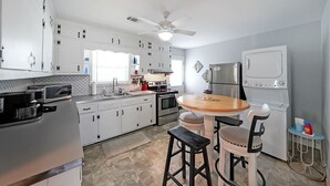 Uma cozinha moderna com armários brancos, uma ilha central, um ventilador de teto e um forno embutido.