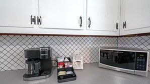 Cozinha com armários brancos, cafeteira Keurig, micro-ondas Frigidaire e um espaço para café com xícaras e uma placa.