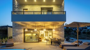 A modern two-story building with a pool, outdoor seating, and a dining area. - Feli Living - luxury villa Chania Crete Greece (Spilia)