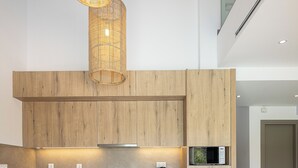 A modern kitchen with wooden cabinetry, a built-in oven, and a hanging light fixture. - Feli Living - luxury villa Chania Crete Greece (Spilia)