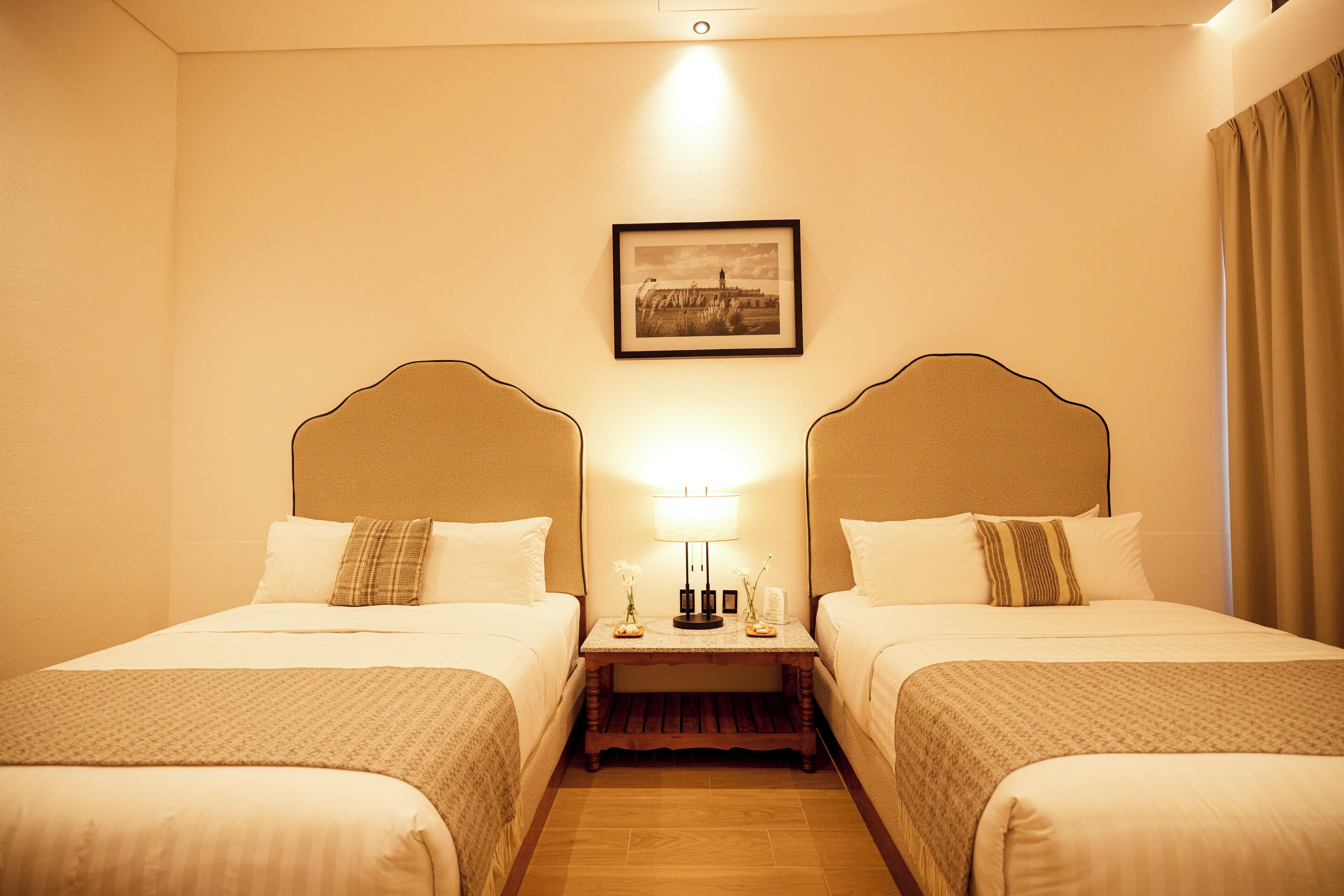 A hotel room with two beds, a nightstand with a lamp, and a framed picture on the wall.