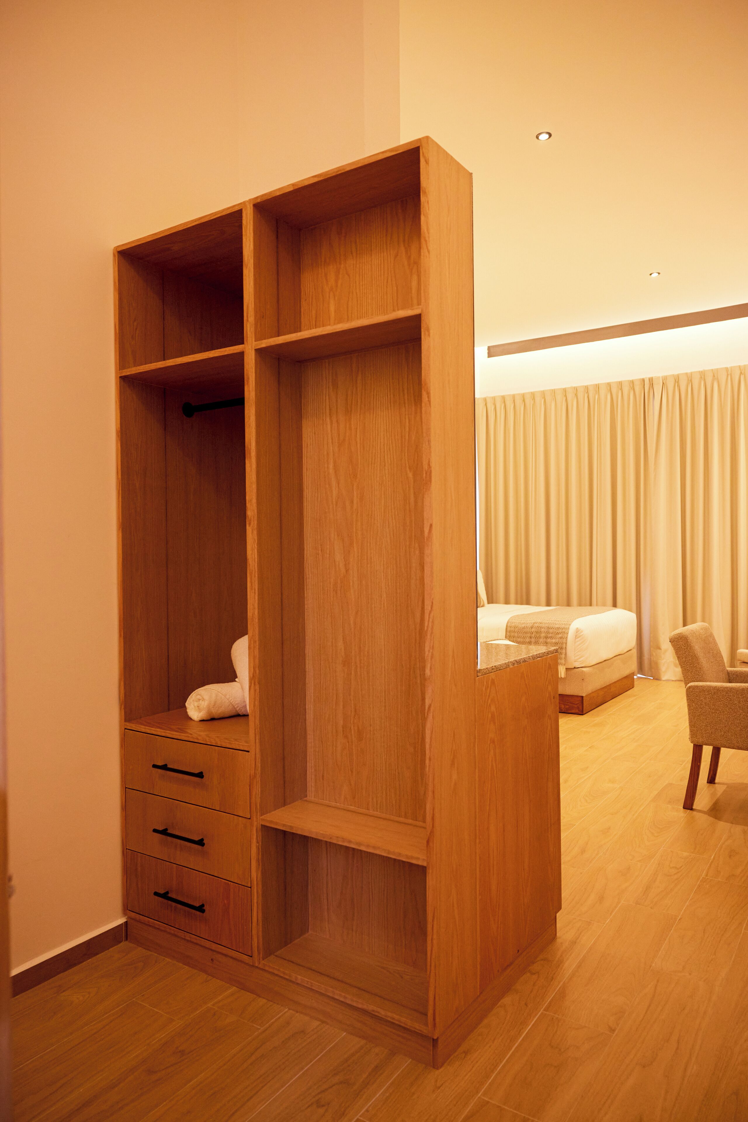 A bedroom with a wooden wardrobe, a bed, and a chair.