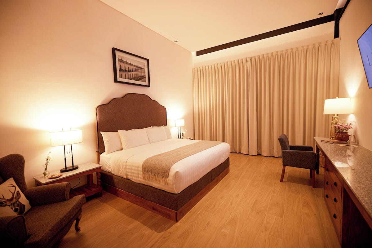 A hotel room with a large bed, a desk, a chair, a lamp, and a TV on the wall.