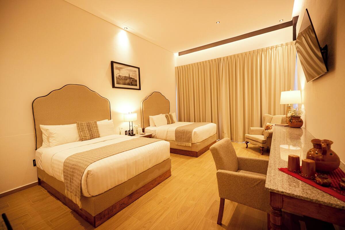 A hotel room with two beds, a desk, a chair, and a TV mounted on the wall.