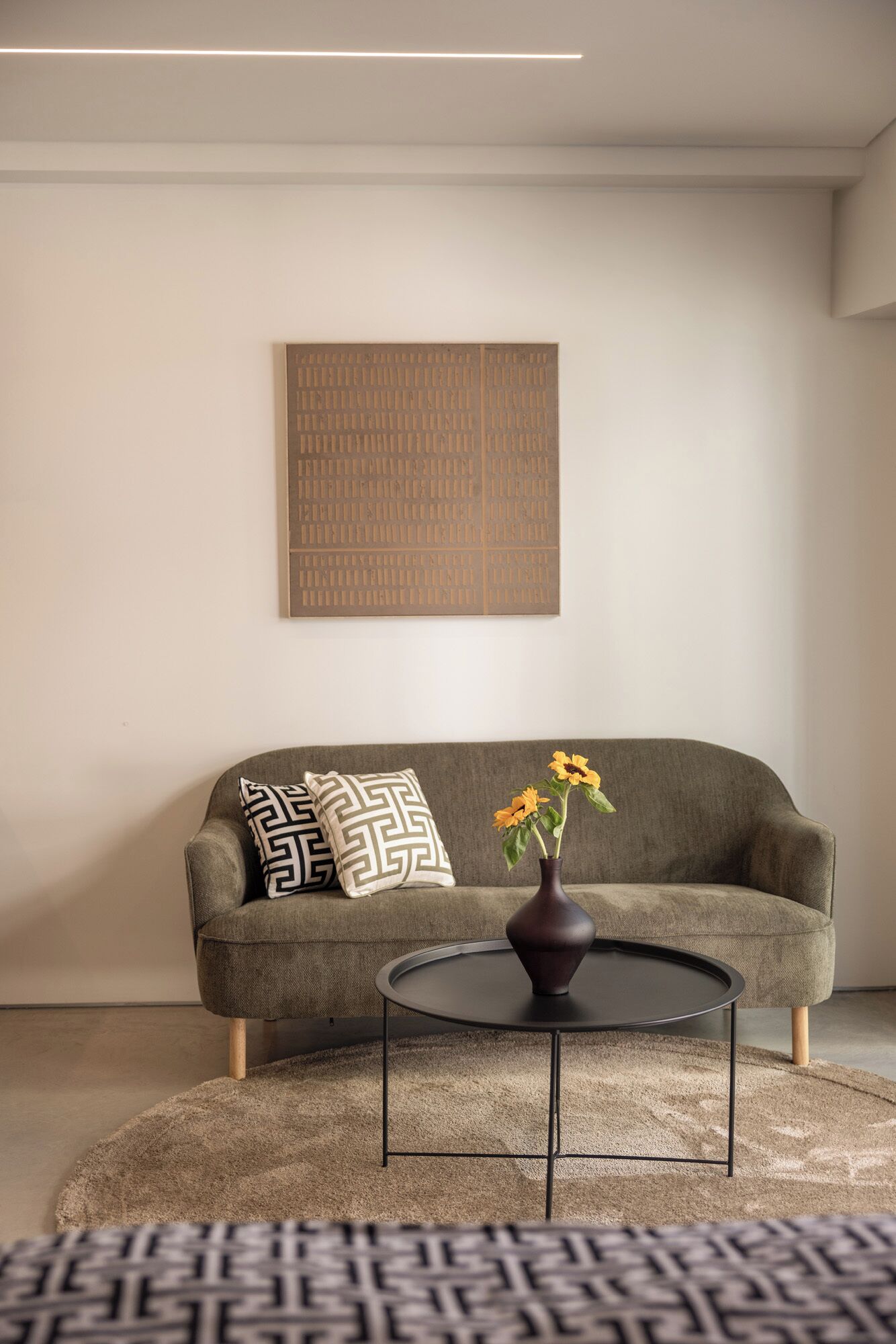 A living room with a sofa, a round coffee table, a vase with flowers, and a patterned rug.