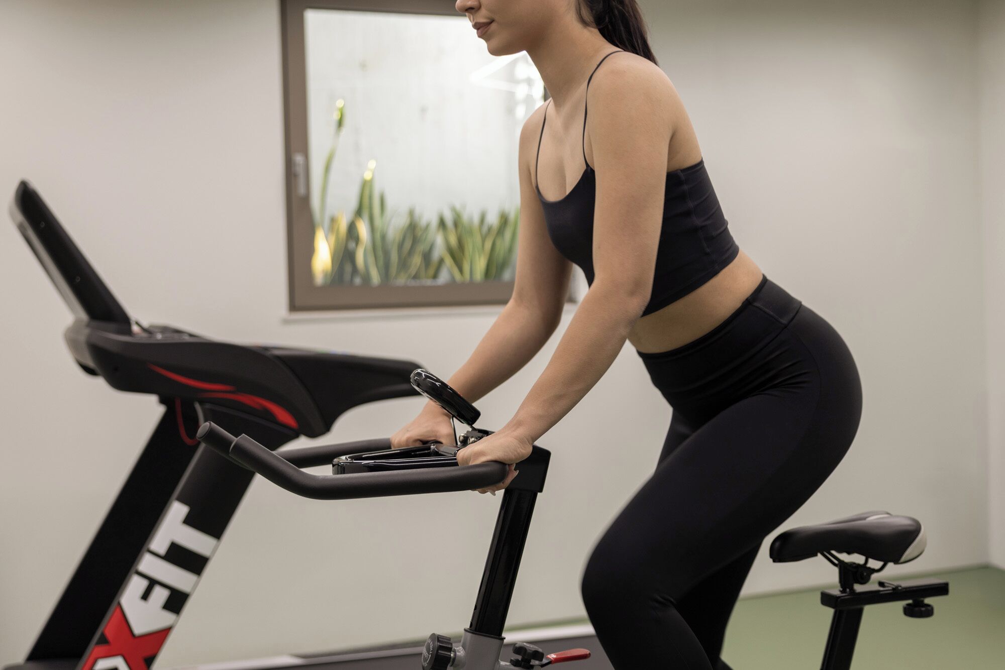 A woman using a stationary bike in a room with a framed picture on the wall.