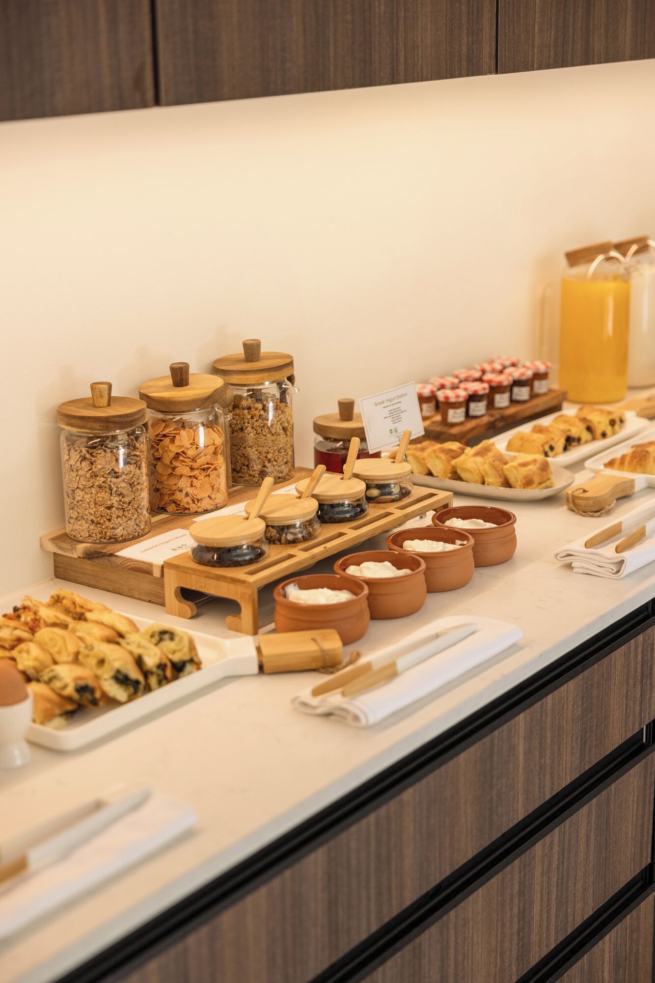 A buffet with various food items, including jars of granola and spreads, arranged on a counter.