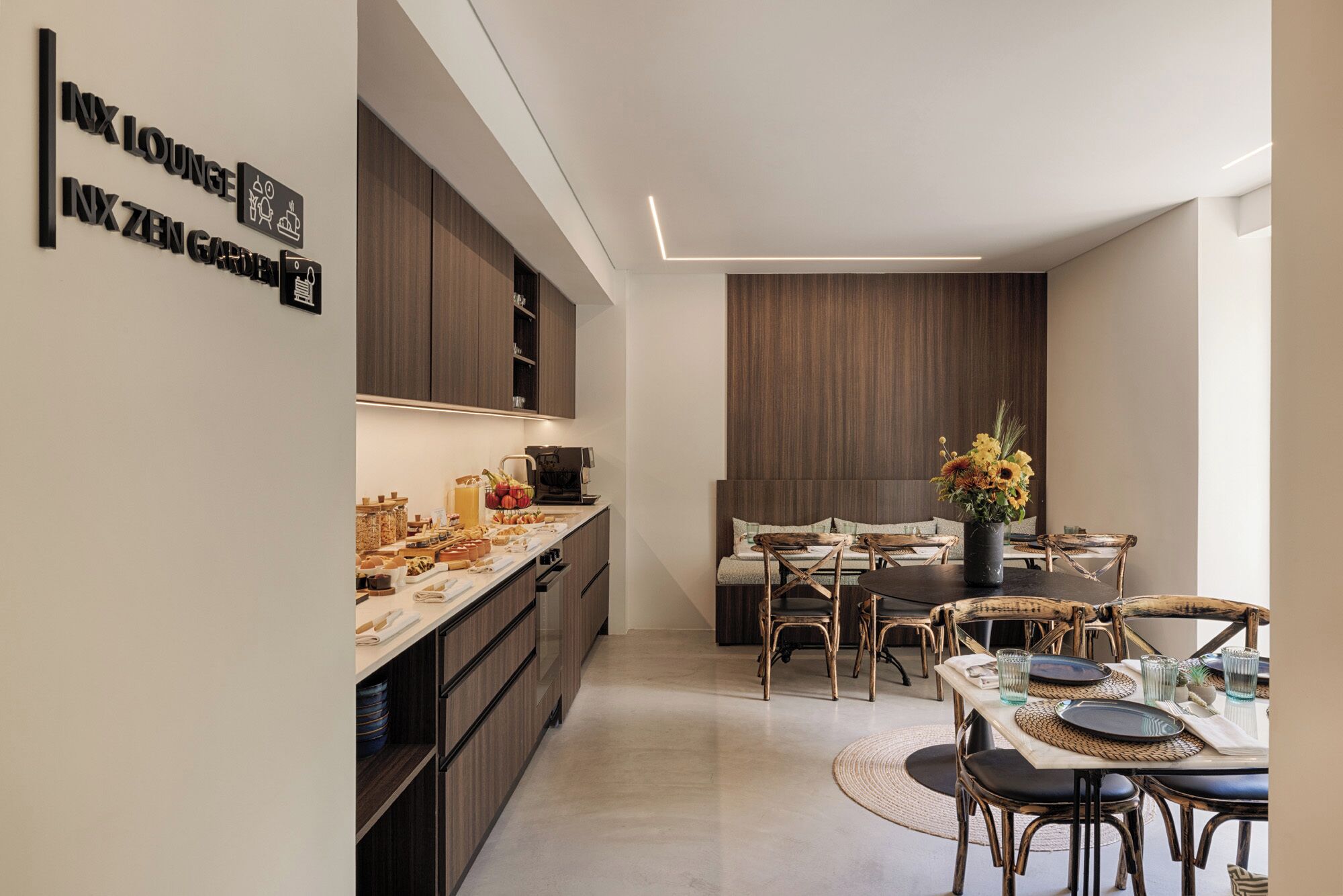 Una cocina moderna con barra desayunadora, armarios de madera y un comedor con sillas de mimbre y una mesa preparada para dos.