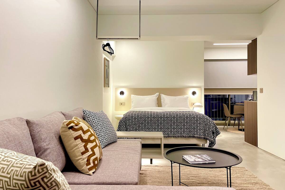 Quarto de hotel moderno com cama, sofá e uma pequena mesa redonda.