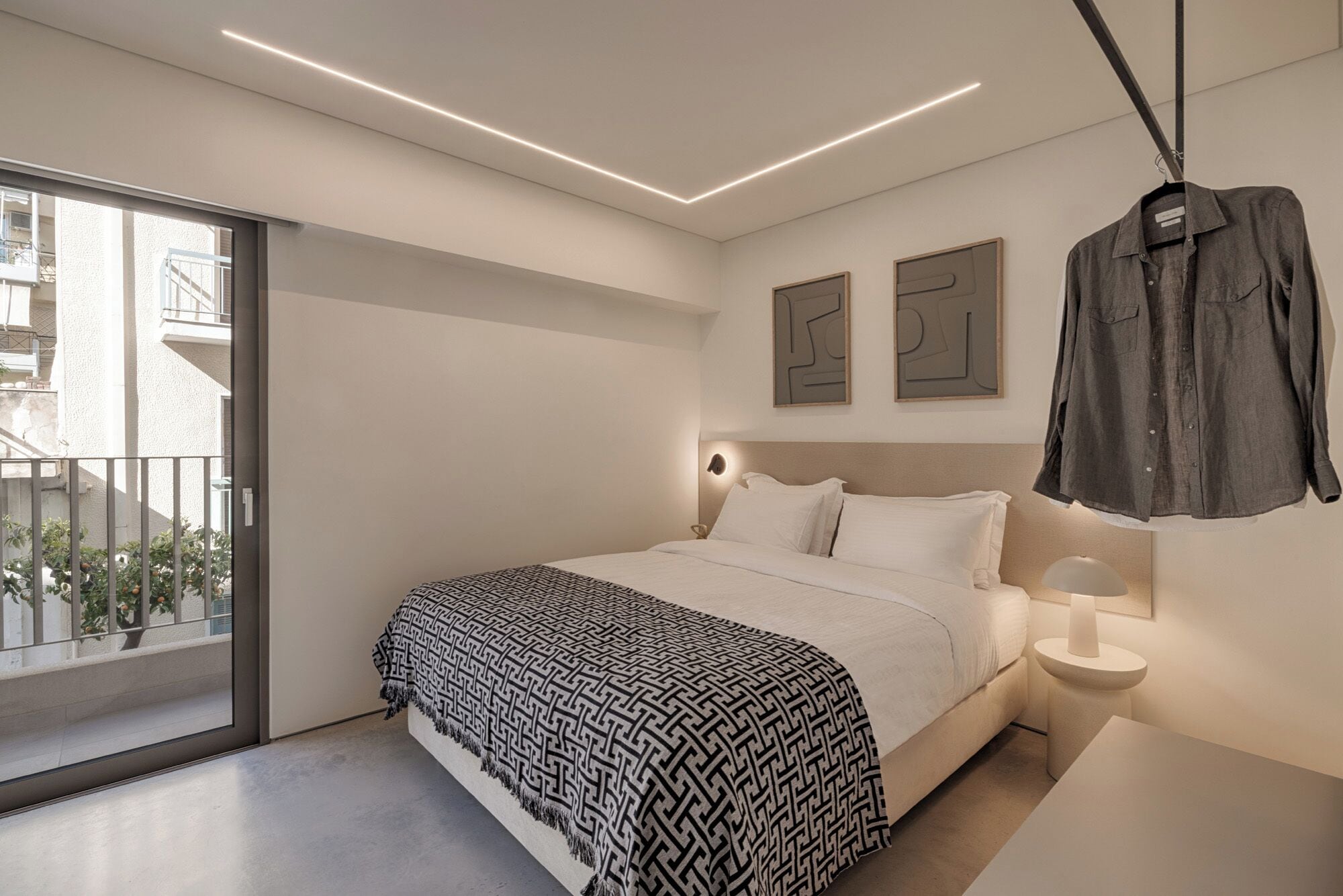 A modern bedroom with a bed, bedside table, and a hanging shirt.