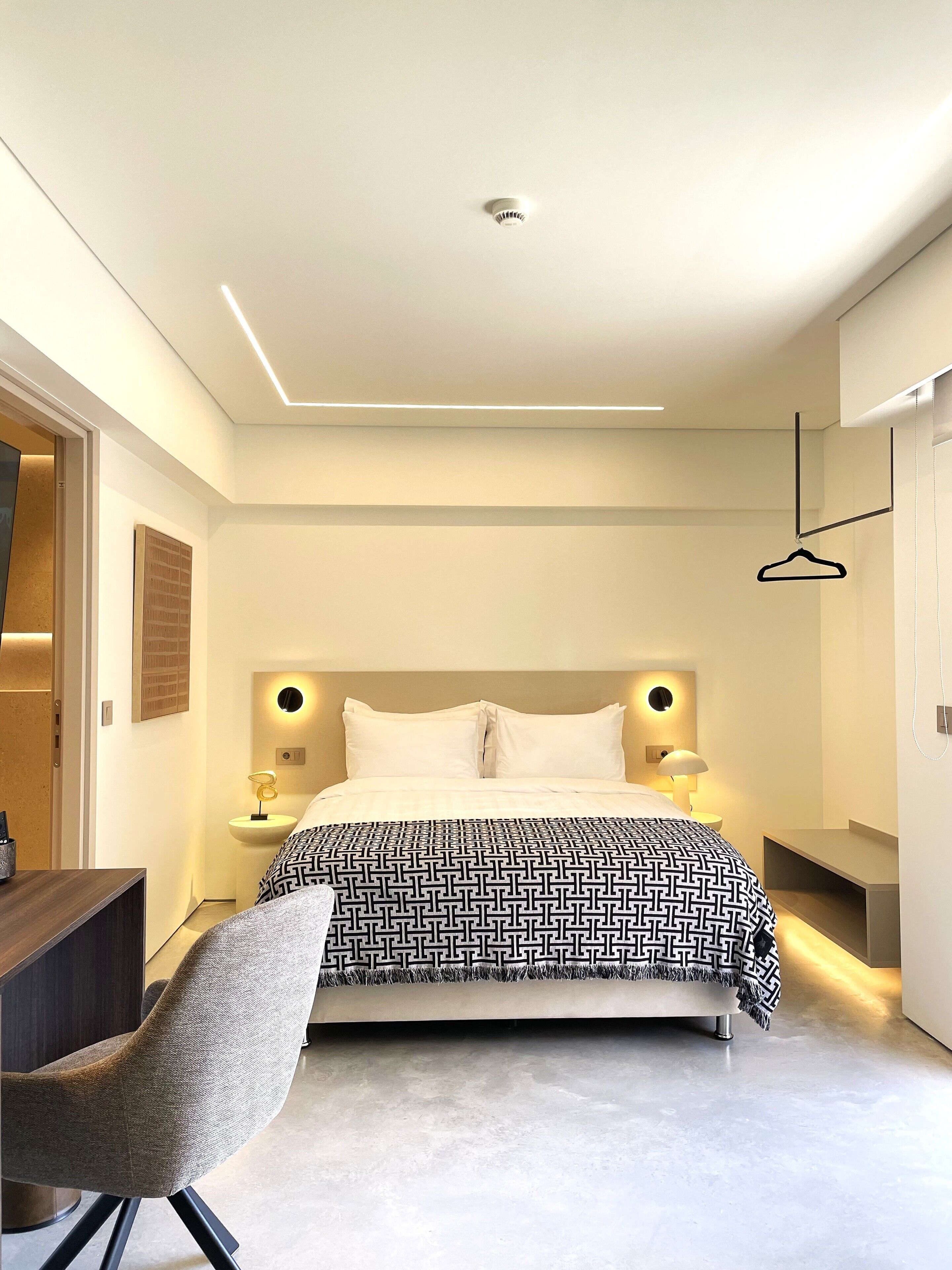 Ein modernes Schlafzimmer mit Bett, Nachttischen, einem Sessel und einer Pendelleuchte.