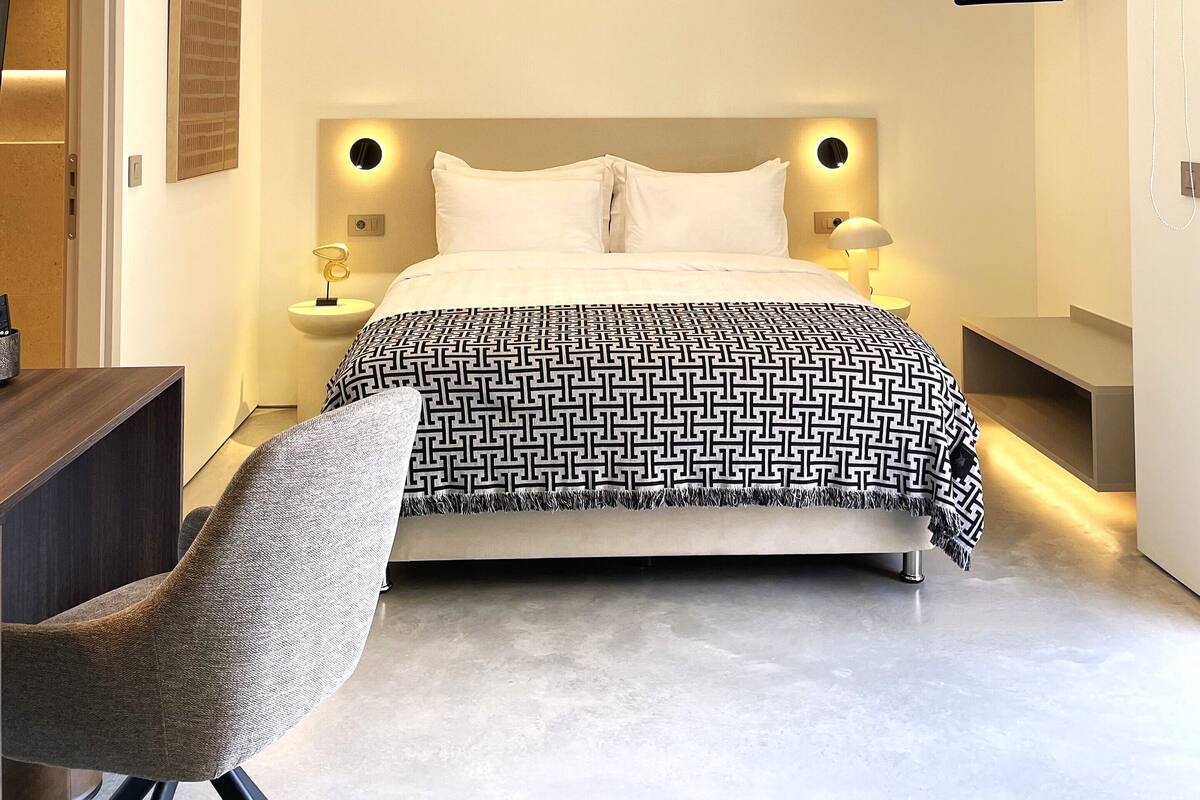 Um quarto moderno com cama, mesas de cabeceira, uma cadeira e um lustre.