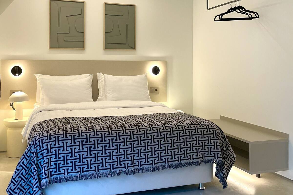 Quarto moderno com cama, mesas de cabeceira, luminária na parede e arte abstrata na parede.