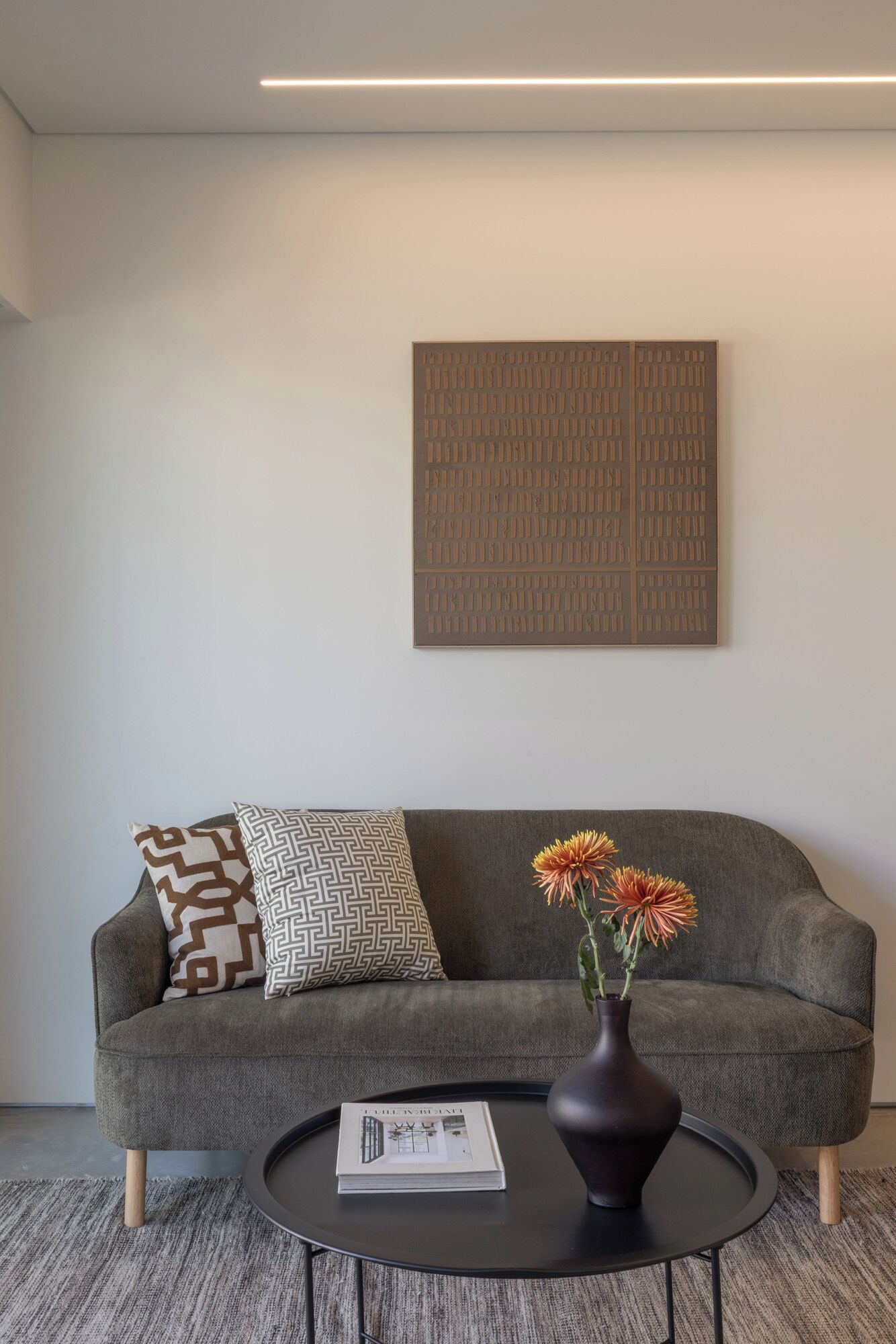 A modern living room with a grey sofa, patterned pillows, a round black coffee table, a vase with flowers, and a large abstract artwork on the wall.