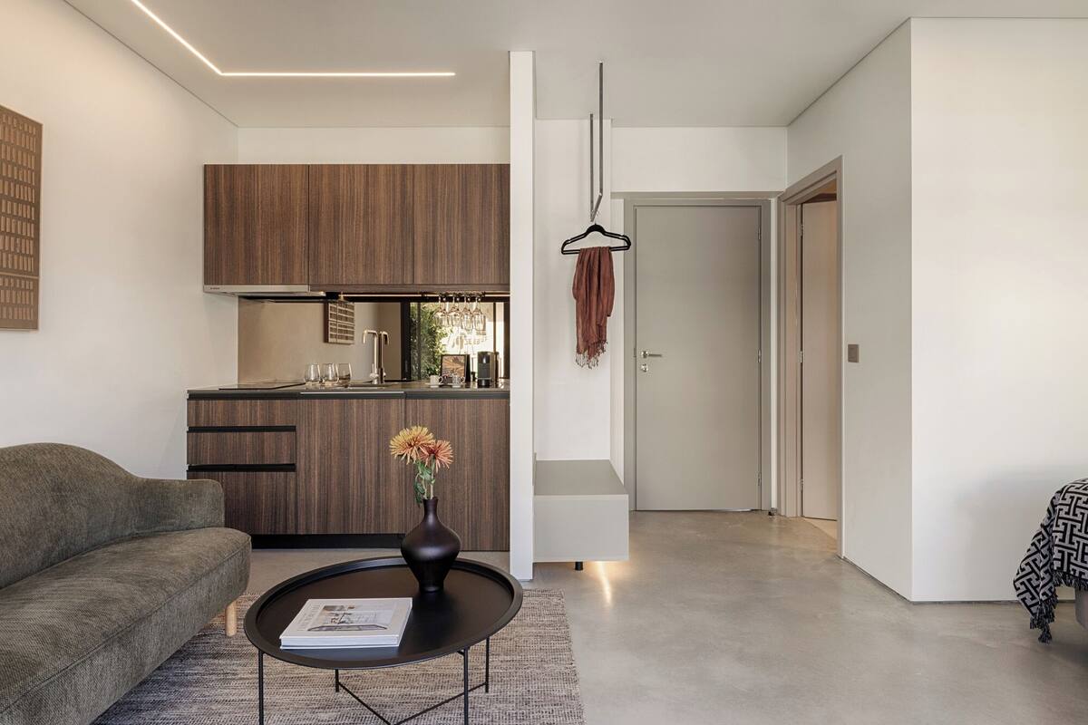 Uma sala de estar moderna com sofá, mesa de centro e cozinha com armários de madeira e luminária pendente.