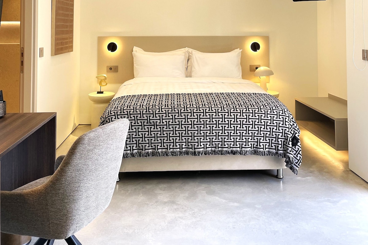 Ein modernes Schlafzimmer mit Bett, Nachttischen, einem Sessel und einer Pendelleuchte.