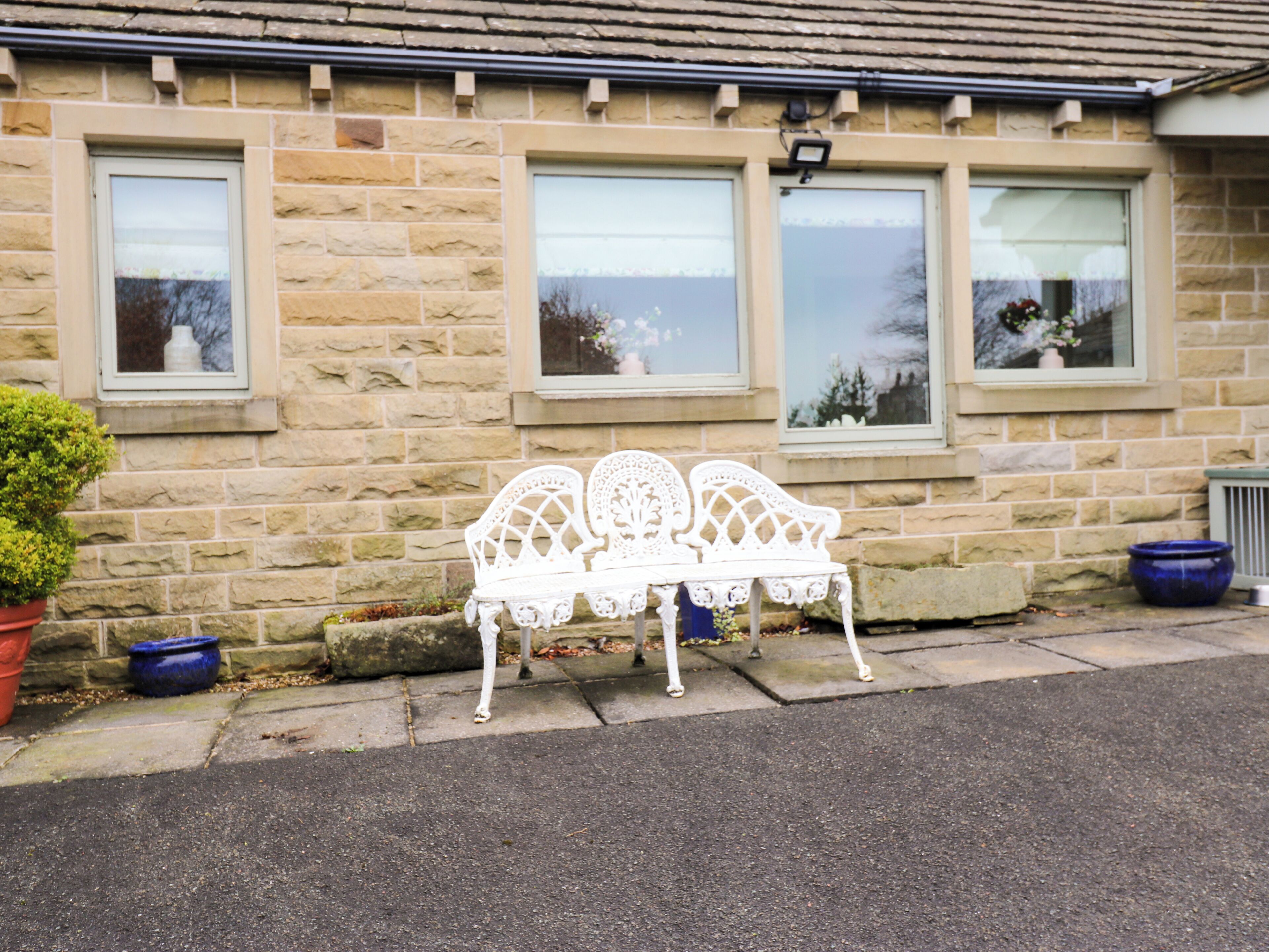A white bench outside a stone building with three windows.