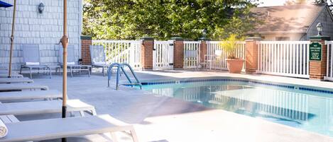 A swimming pool with lounge chairs and umbrellas, surrounded by a white fence and trees.