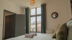 Ein Schlafzimmer mit einem Bett, zwei gerollten Handtüchern, einem Fenster mit Vorhängen, einem Spiegel und einer Tür.
